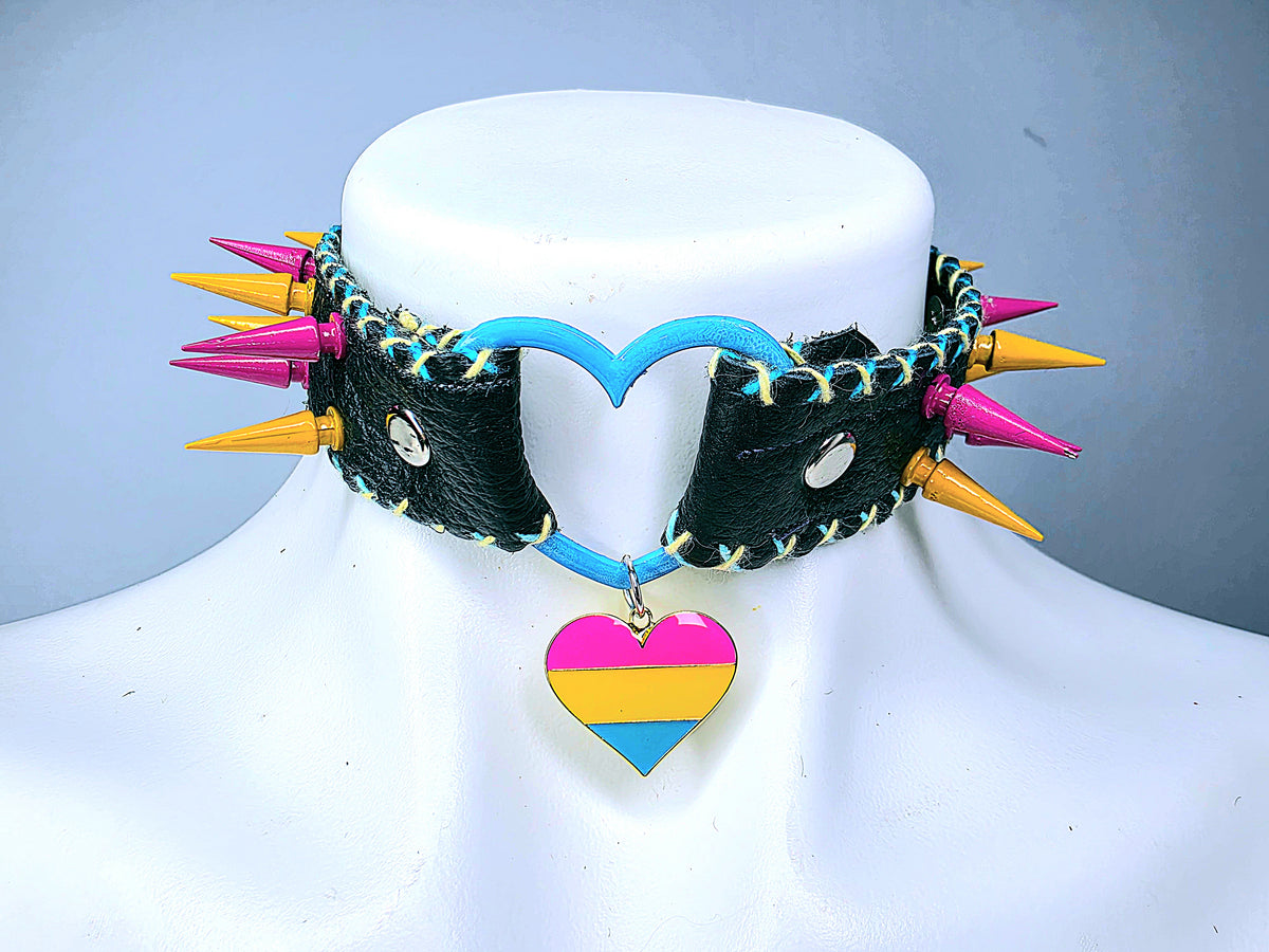 "Handmade black leather pansexual pride collar with pink and yellow spikes, blue heart charm, and blue and yellow embroidered edges"